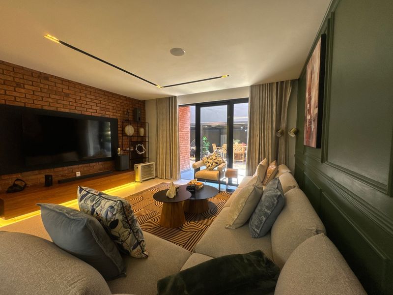 Modern living room featuring an exposed brick wall, custom wainscoting, recessed linear lighting, and large sliding doors opening to an outdoor patio area.