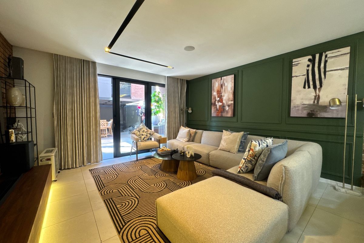 Modern living room featuring a dark green wainscoted feature wall, recessed linear lighting, tiled floors, and large sliding glass doors leading to an outdoor area.