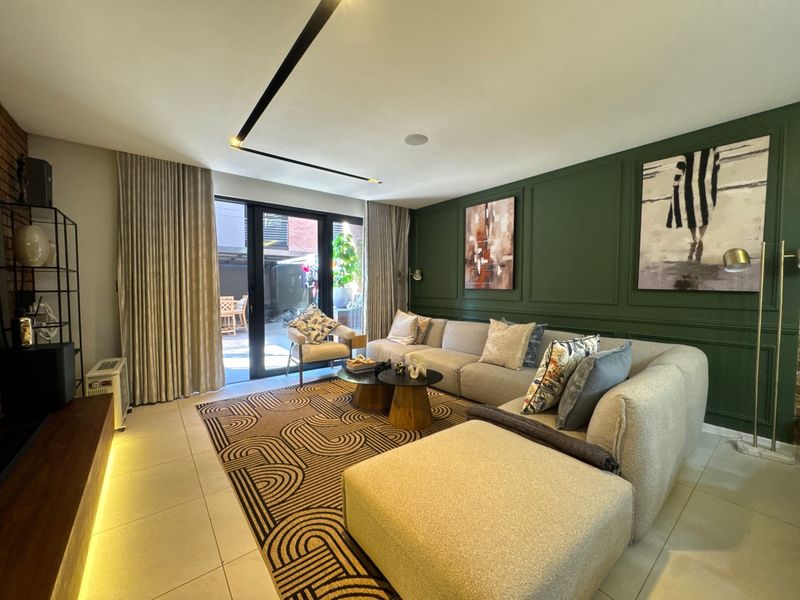 Modern living room featuring a dark green wainscoted feature wall, recessed linear lighting, tiled floors, and large sliding glass doors leading to an outdoor area.