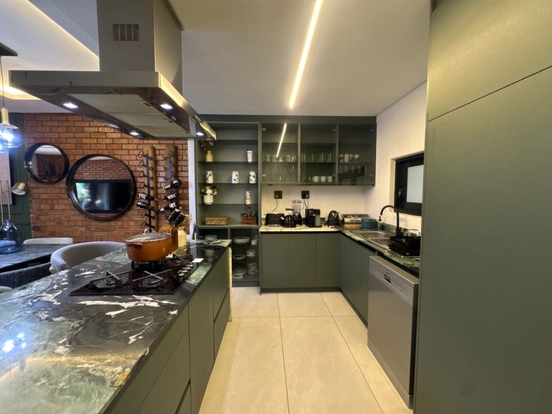 Modern kitchen featuring a stone island with gas hob, sleek green cabinetry, integrated shelving, and an exposed brick feature wall.