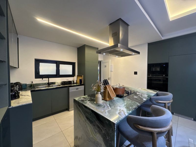 Modern kitchen featuring dark green cabinetry, a striking stone-topped island with integrated cooktop, stainless steel extractor fan, and high-end finishes throughout.