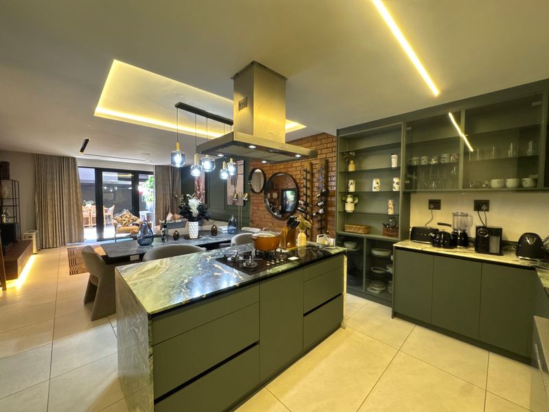 Modern open-plan kitchen and living area featuring a central island with stone countertop, sleek cabinetry, exposed brick accents, and contemporary recessed lighting.