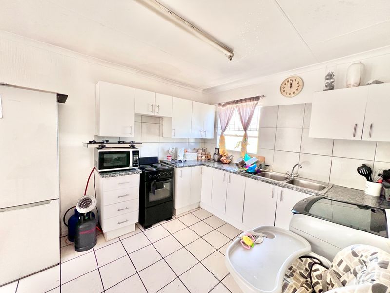 A functional kitchen featuring white cabinetry, laminate countertops, a double basin sink, and tiled flooring with a tiled backsplash.