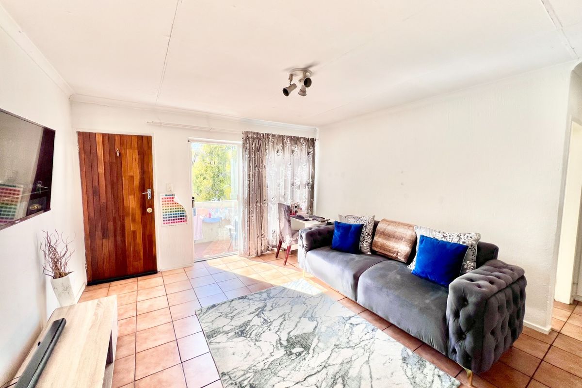 A living room featuring tiled flooring, a wooden entrance door, and a sliding glass door leading to an outdoor area.