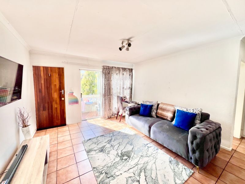 A living room featuring tiled flooring, a wooden entrance door, and a sliding glass door leading to an outdoor area.