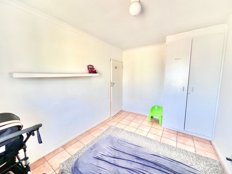 A bedroom featuring tiled flooring, built-in cupboards, and a ceiling light fixture, offering a functional space ready for personalization.