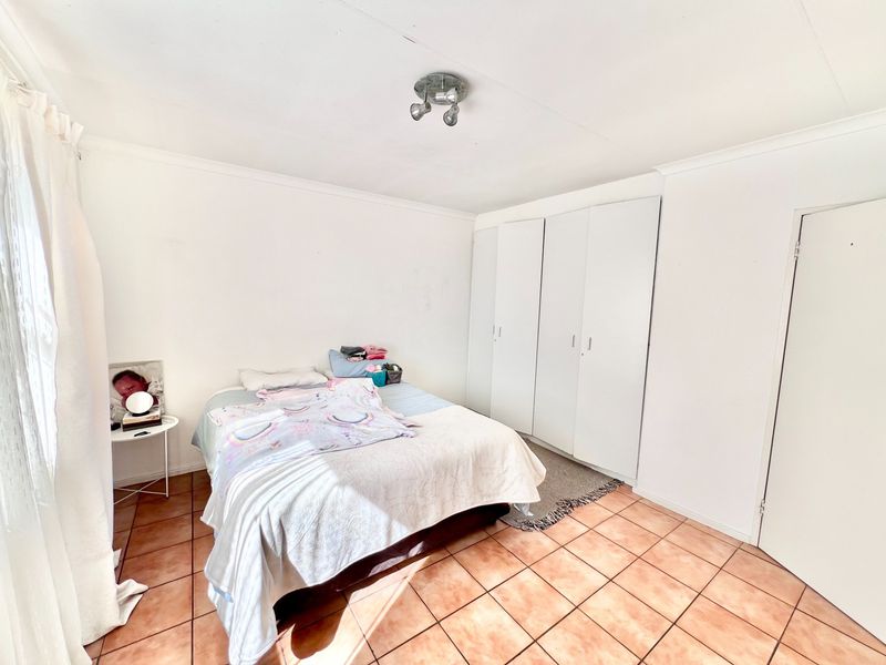 A functional bedroom featuring tiled flooring, built-in cupboards, and a ceiling-mounted spotlight fixture, offering a clean and neutral space.