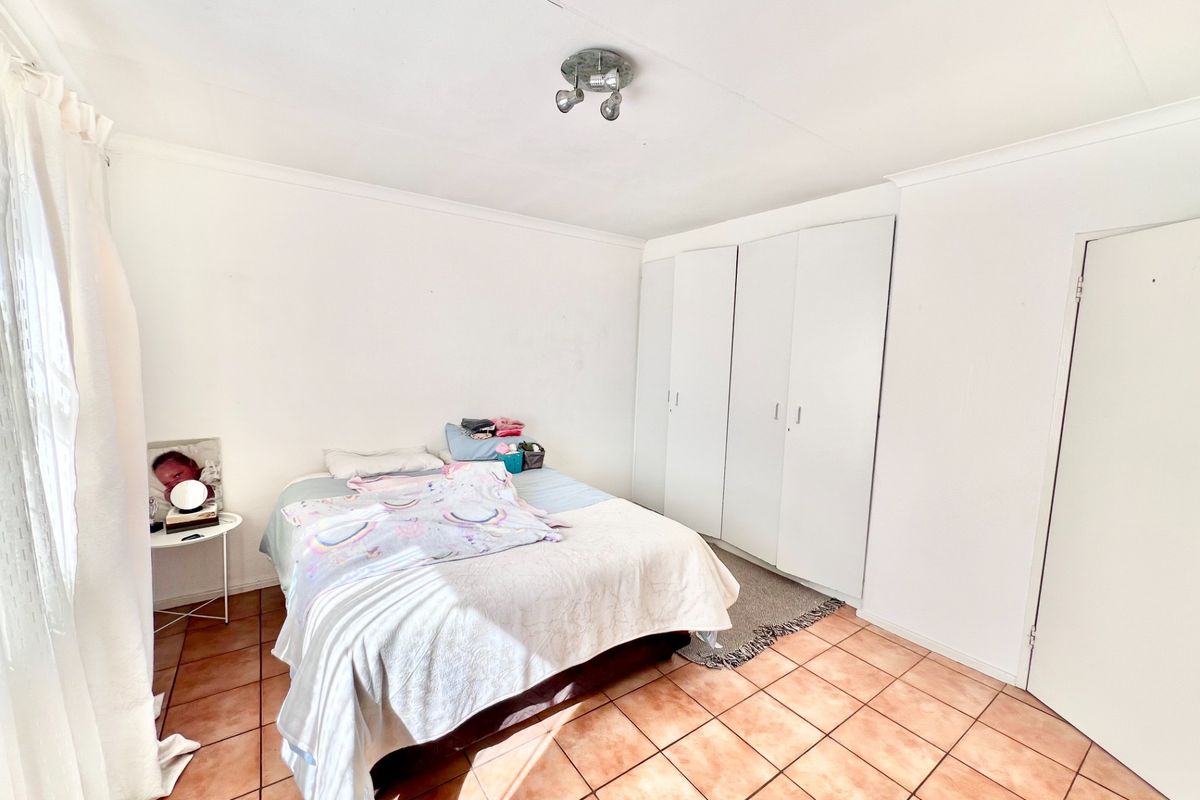 A functional bedroom featuring tiled flooring, built-in cupboards, and a ceiling-mounted spotlight fixture, offering a clean and neutral space.
