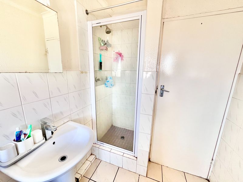 A functional bathroom featuring a pedestal basin, a tiled shower enclosure, and neutral wall tiling throughout.