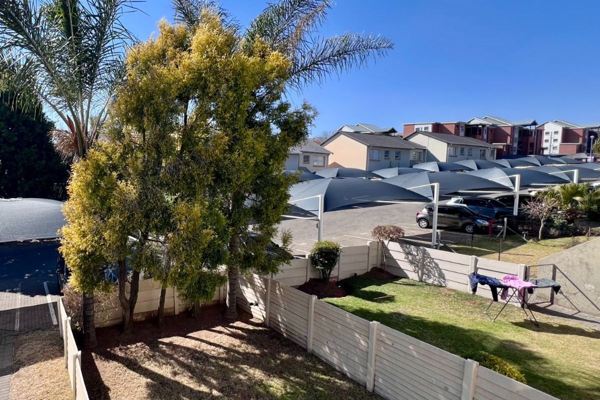 A view of the rear garden area featuring a lawn and precast concrete boundary wall, overlooking the complex parking area with shade cloth carports.