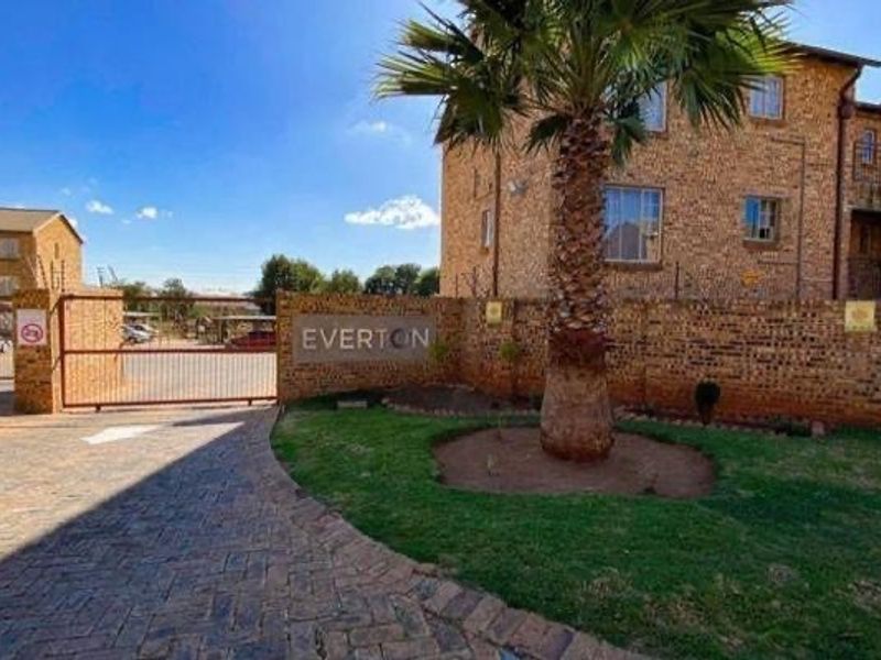Front entrance view of the Everton townhouse complex featuring a paved driveway, secure gated access, and established garden landscaping.