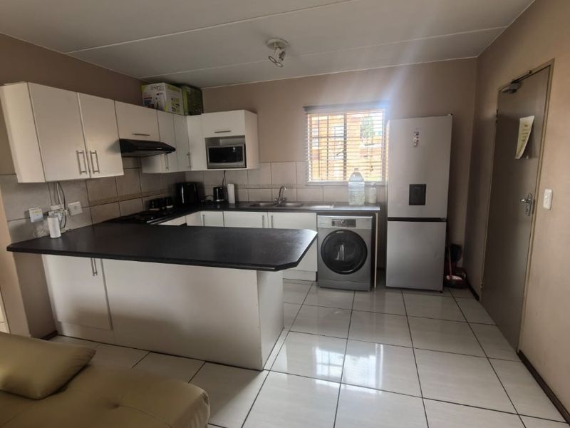 Open-plan kitchen featuring white cabinetry, dark countertops, tiled flooring, and integrated appliances, seamlessly connecting to the living area.