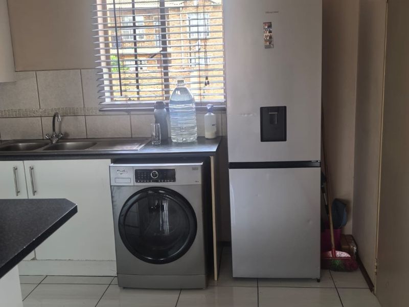 A functional kitchen area featuring white cabinetry, a double sink, tiled backsplash, and tiled flooring, with space for laundry and refrigeration appliances.