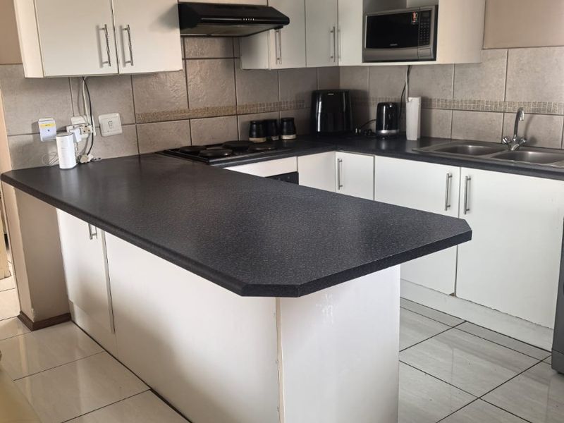 Functional kitchen featuring white cabinetry, dark laminate countertops, tiled backsplash, and built-in appliances, offering a practical layout for daily meal preparation.