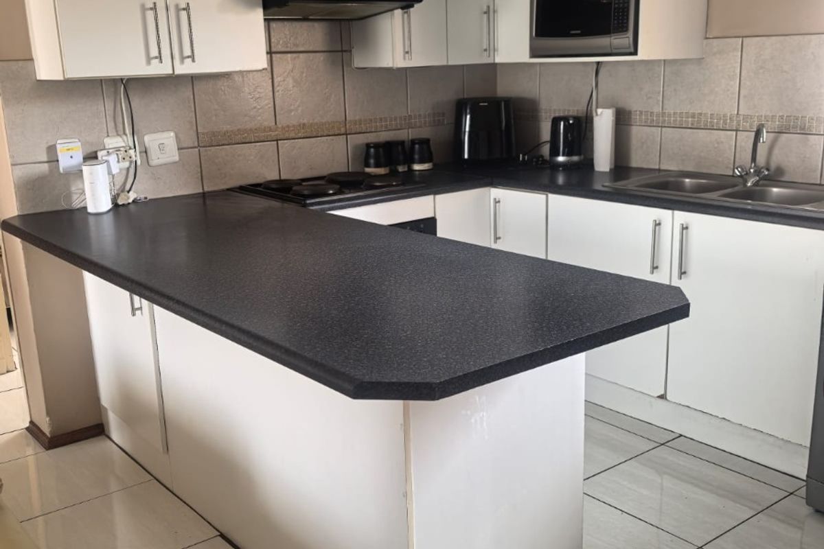 Functional kitchen featuring white cabinetry, dark laminate countertops, tiled backsplash, and built-in appliances, offering a practical layout for daily meal preparation.