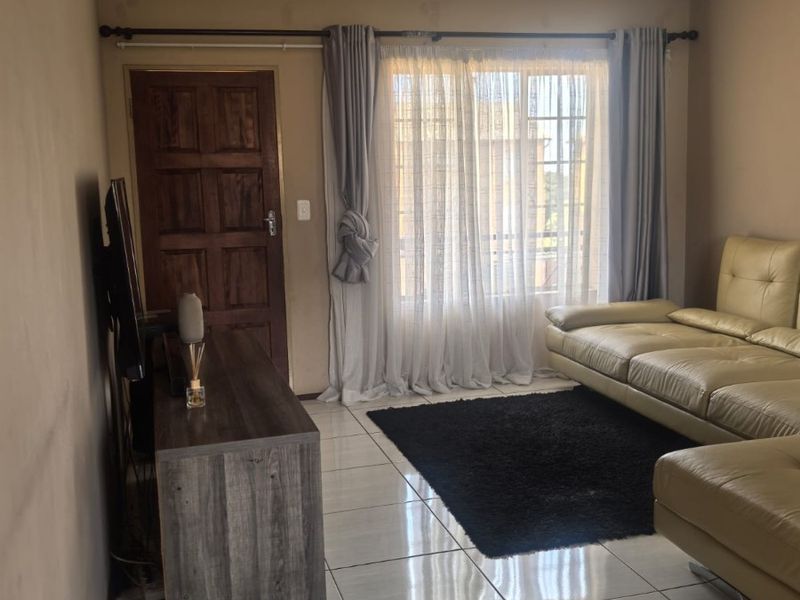 A living room featuring tiled flooring, a timber panel door, and a window with curtain fixtures.