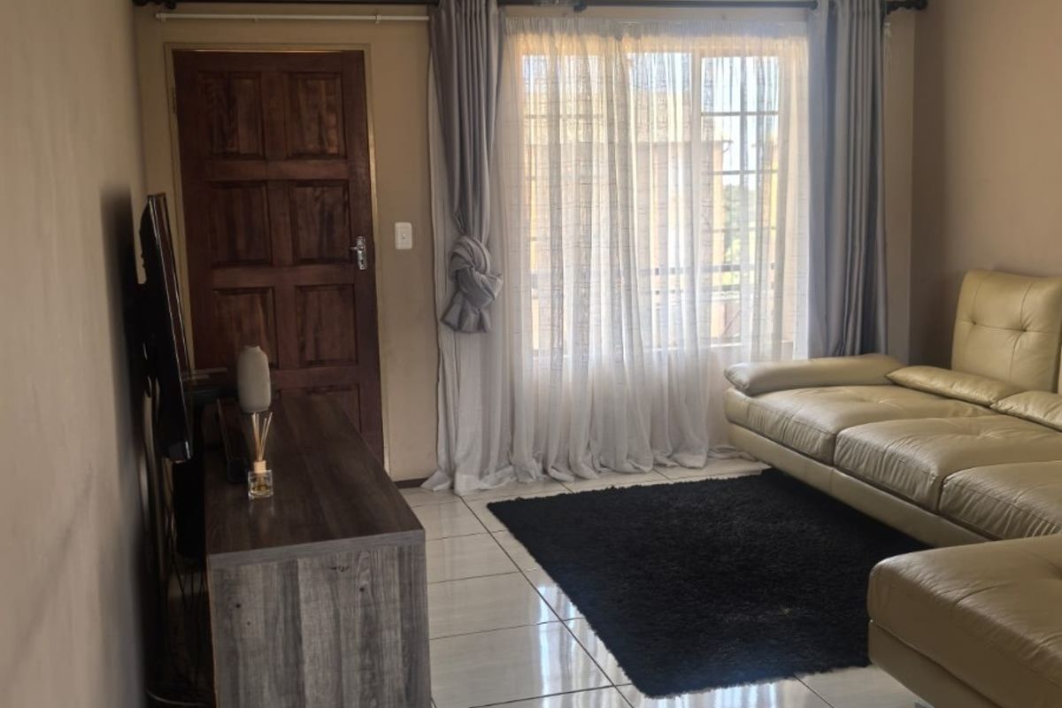 A living room featuring tiled flooring, a timber panel door, and a window with curtain fixtures.