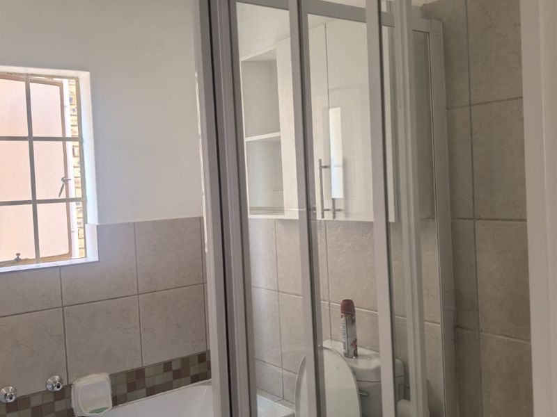 A functional bathroom featuring a built-in bathtub, a separate shower enclosure, a toilet, and wall-mounted storage cabinetry with neutral tiled finishes.