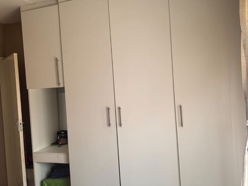 A bedroom featuring white built-in cupboards with integrated vanity space and overhead storage units.