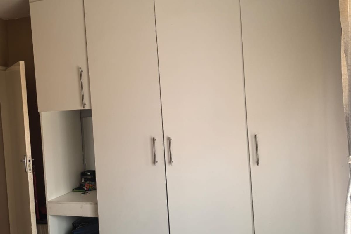 A bedroom featuring white built-in cupboards with integrated vanity space and overhead storage units.
