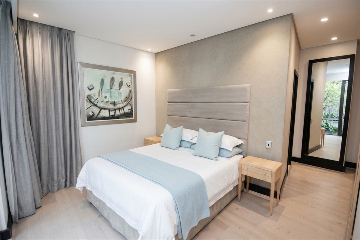 A modern, well-maintained bedroom featuring light timber flooring, a textured feature wall, recessed downlighting, and a full-length mirror.