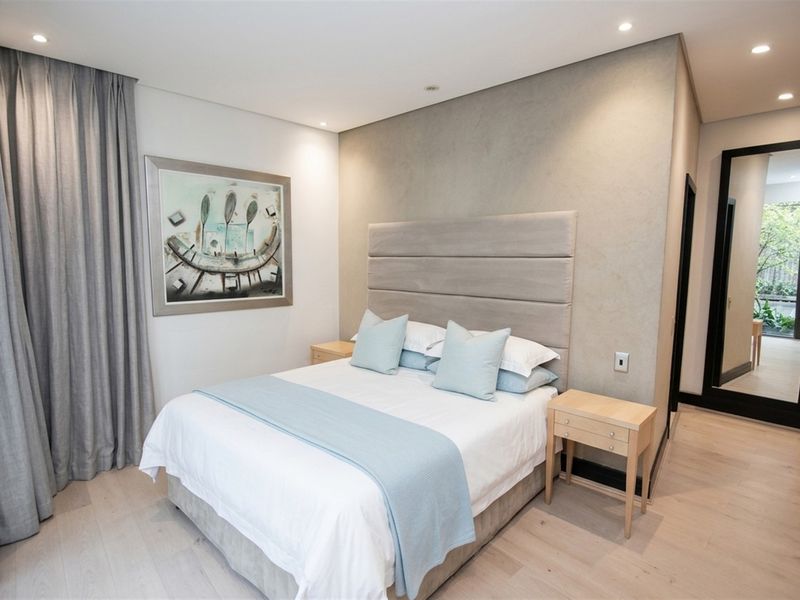 A modern, well-maintained bedroom featuring light timber flooring, a textured feature wall, recessed downlighting, and a full-length mirror.