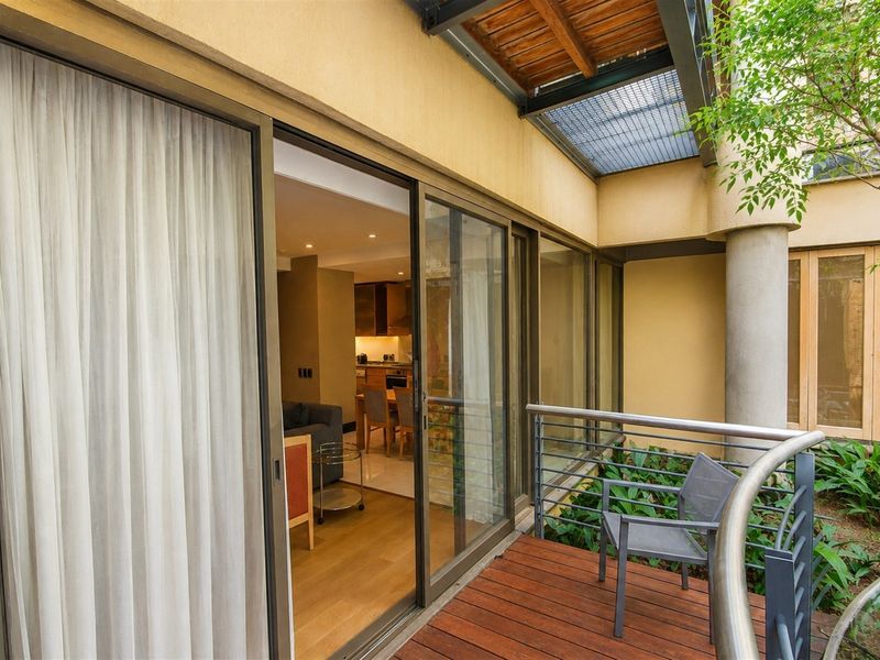 A covered balcony featuring timber decking, metal railings, and sliding glass doors providing seamless access to the interior living space.