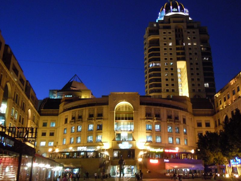 Night view of a large multi-story apartment complex featuring an arched entrance, illuminated facade, and surrounding urban infrastructure.