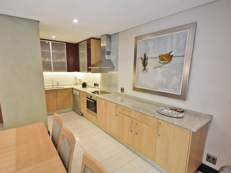 Modern kitchen featuring light wood cabinetry, granite countertops, integrated stainless steel appliances, and tiled flooring with recessed lighting.