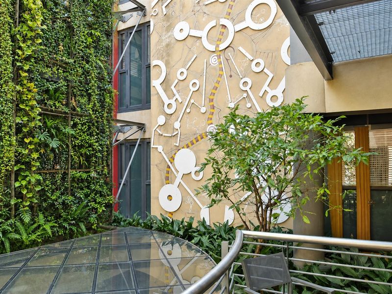 A well-maintained courtyard area featuring a vertical garden, decorative wall mural, and a modern glass canopy structure.