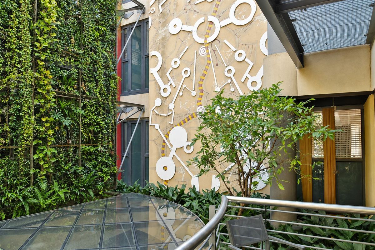 A well-maintained courtyard area featuring a vertical garden, decorative wall mural, and a modern glass canopy structure.