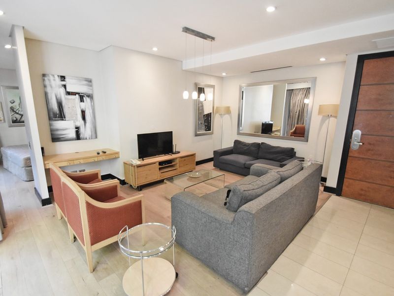 A well-maintained living room featuring a mix of laminate and tiled flooring, recessed lighting, and a built-in desk area near the entrance.