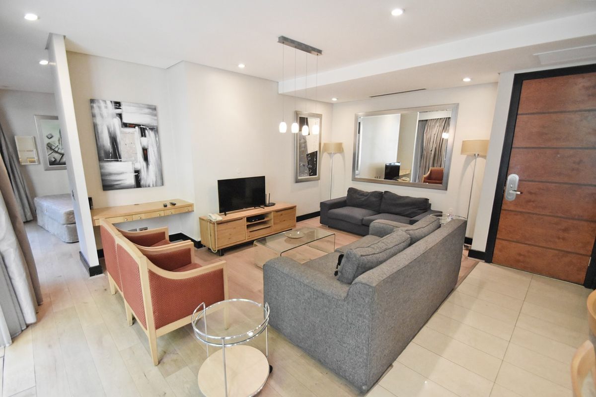 A well-maintained living room featuring a mix of laminate and tiled flooring, recessed lighting, and a built-in desk area near the entrance.