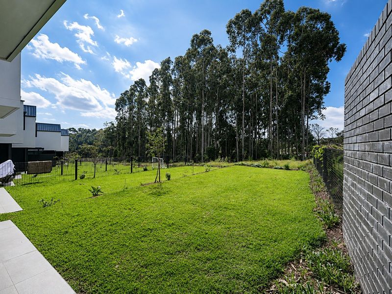 A well-maintained private garden featuring a lush lawn, brick boundary wall, and wire fencing, bordered by tall trees.