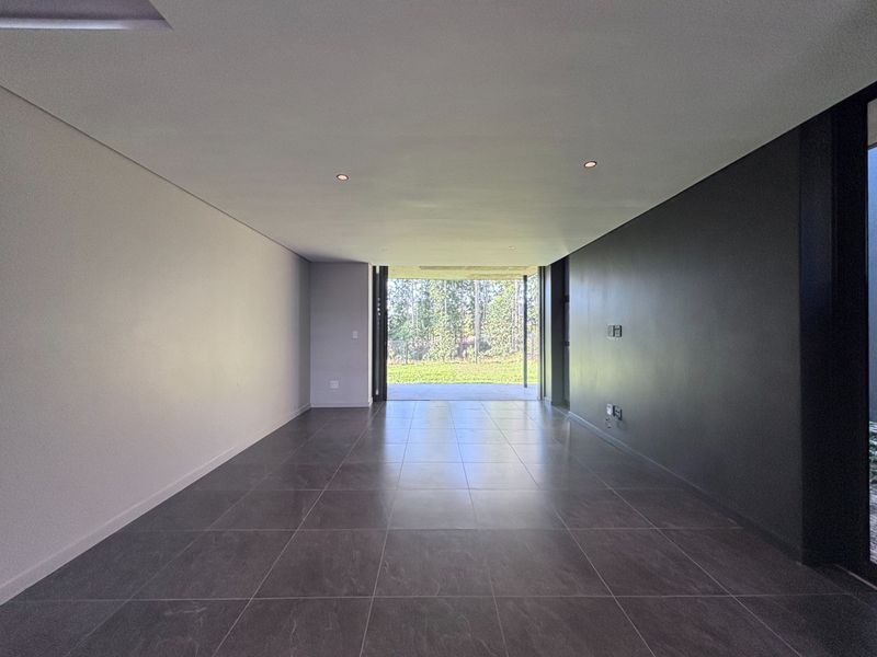 A spacious, modern open-plan living area featuring large format floor tiles, recessed lighting, and seamless access to the outdoor patio through sliding glass doors.