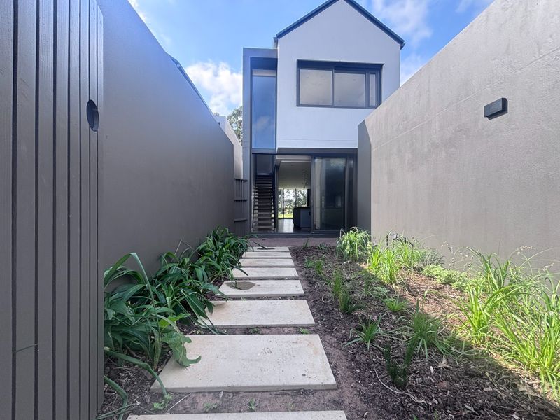 A modern townhouse rear exterior featuring a paved walkway through a landscaped garden leading to a sliding glass door entrance and internal staircase.