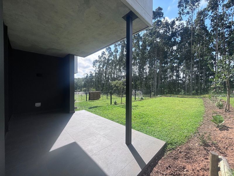 A modern covered patio featuring sleek tiled flooring and a structural steel support column, overlooking a private garden area with mature trees.
