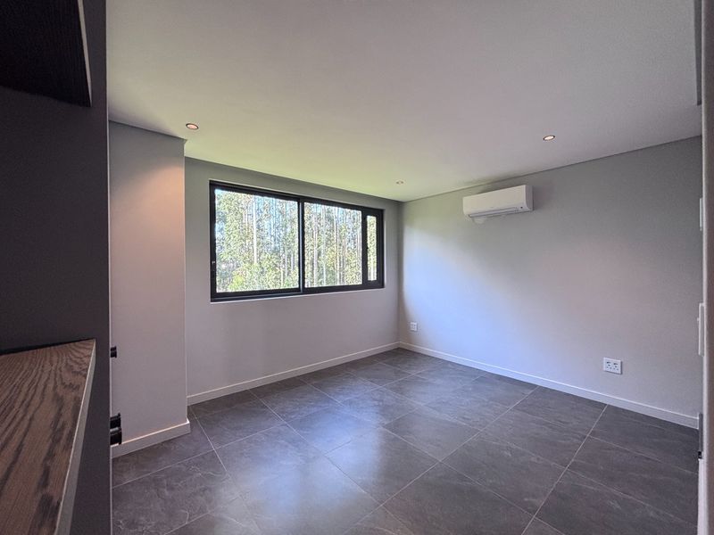 A clean, modern, and empty bedroom featuring large format floor tiles, recessed lighting, and a wall-mounted air conditioning unit.