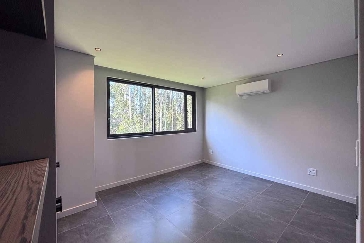 A clean, modern, and empty bedroom featuring large format floor tiles, recessed lighting, and a wall-mounted air conditioning unit.