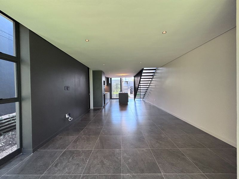 Spacious open-plan living and kitchen area featuring modern dark floor tiles, recessed lighting, and a sleek staircase in a contemporary townhouse setting.