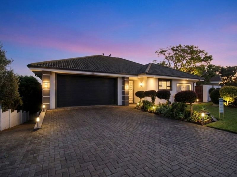 A well-maintained front elevation featuring a paved driveway, double garage, and landscaped garden, illuminated by exterior lighting at dusk.