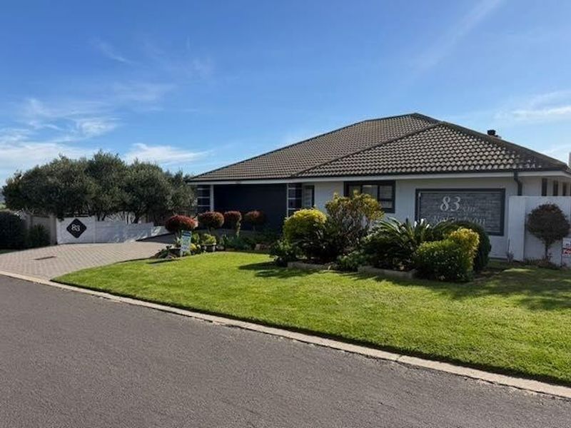 A well-maintained single-story residential property featuring a tiled roof, paved driveway, and established front garden with boundary walling.