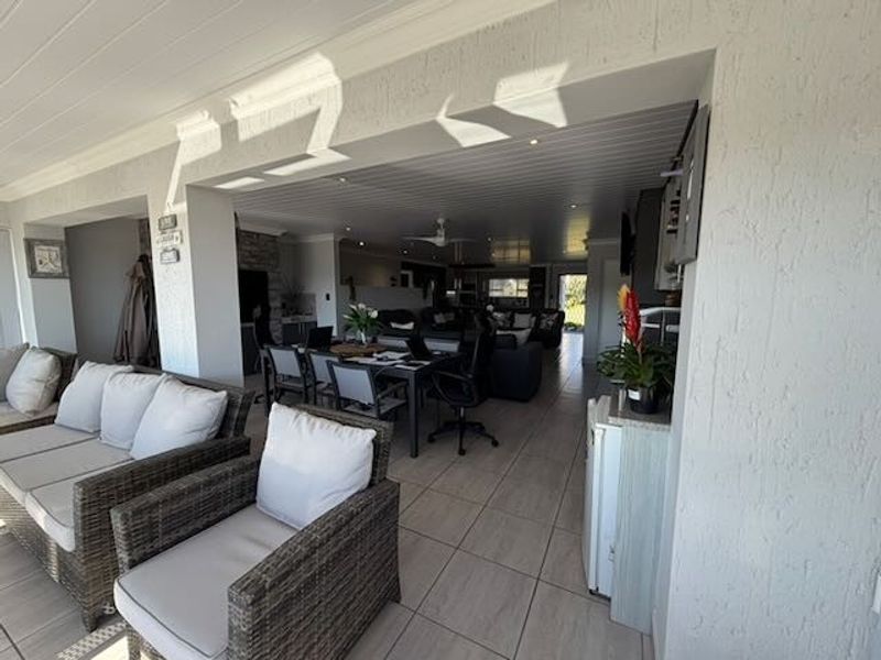 A spacious covered patio area featuring tiled flooring and recessed ceiling lighting, seamlessly connecting to the open-plan interior living and dining spaces.