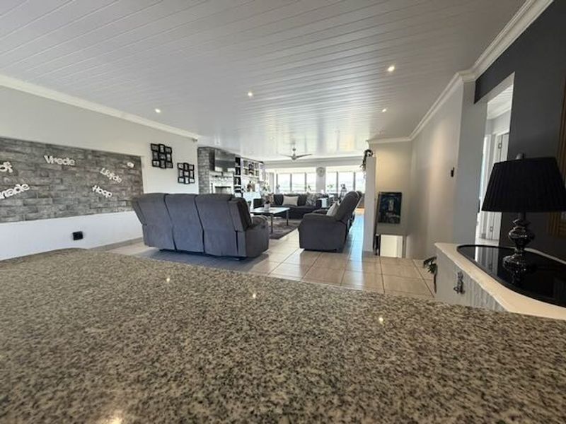 Spacious open-plan living area featuring a granite kitchen island, stone accent wall, and modern tongue and groove ceiling with recessed lighting.