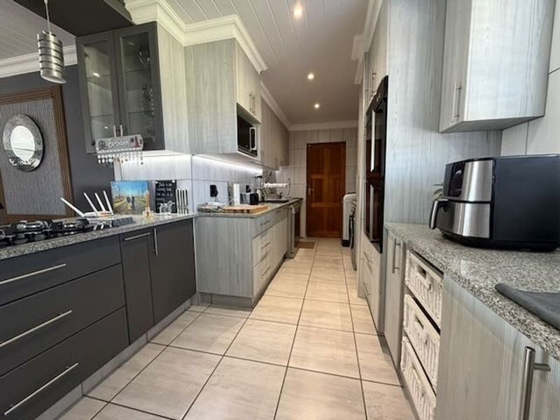 Modern kitchen featuring granite countertops, built-in double oven, gas hob, and ample cabinetry, complemented by tiled flooring and a timber panelled ceiling.