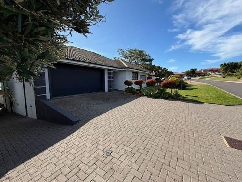 Front exterior view of the property featuring a paved driveway, double garage, and well-maintained landscaped garden.