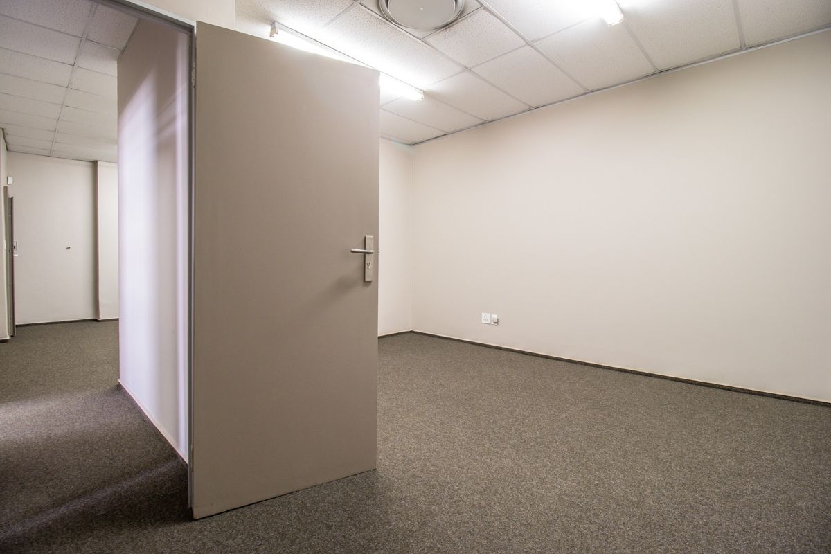 A vacant commercial office space featuring neutral walls, carpeted flooring, and a suspended ceiling with integrated lighting.