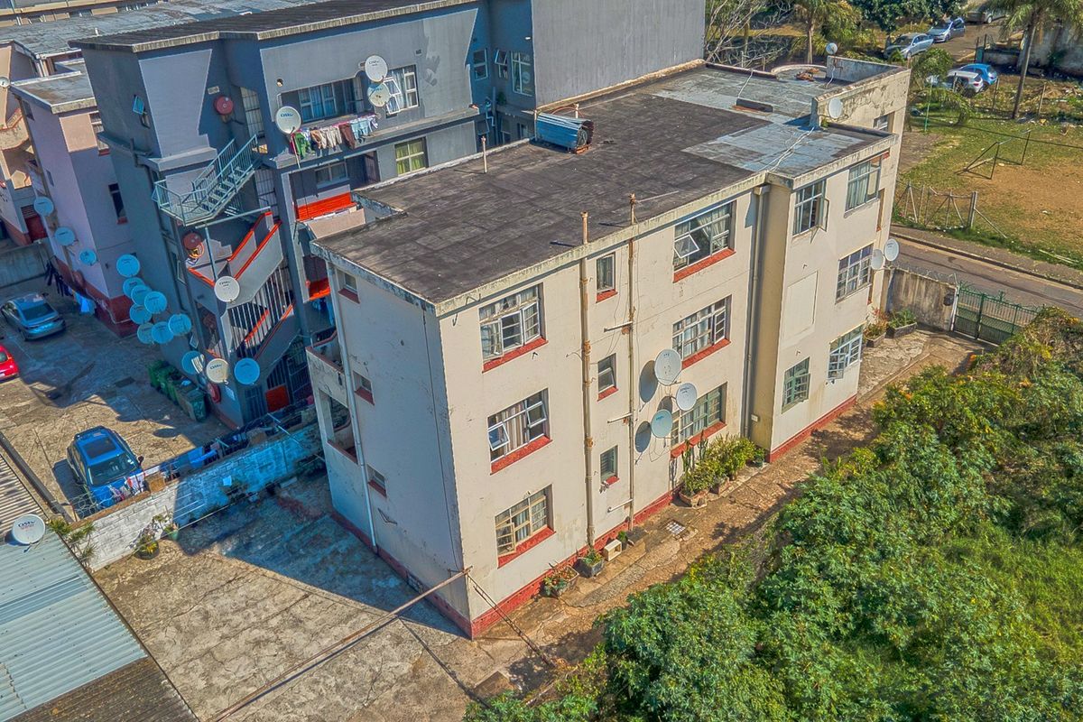 Aerial view of a multi-story apartment building featuring a flat roof, steel-framed windows, and surrounding concrete driveway area.