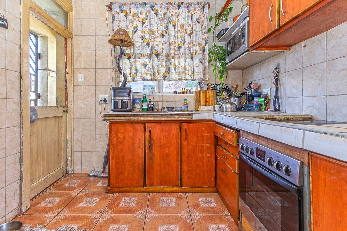 A compact kitchen featuring dated wooden cabinetry, tiled surfaces, and a built-in oven, offering significant potential for a modern renovation.
