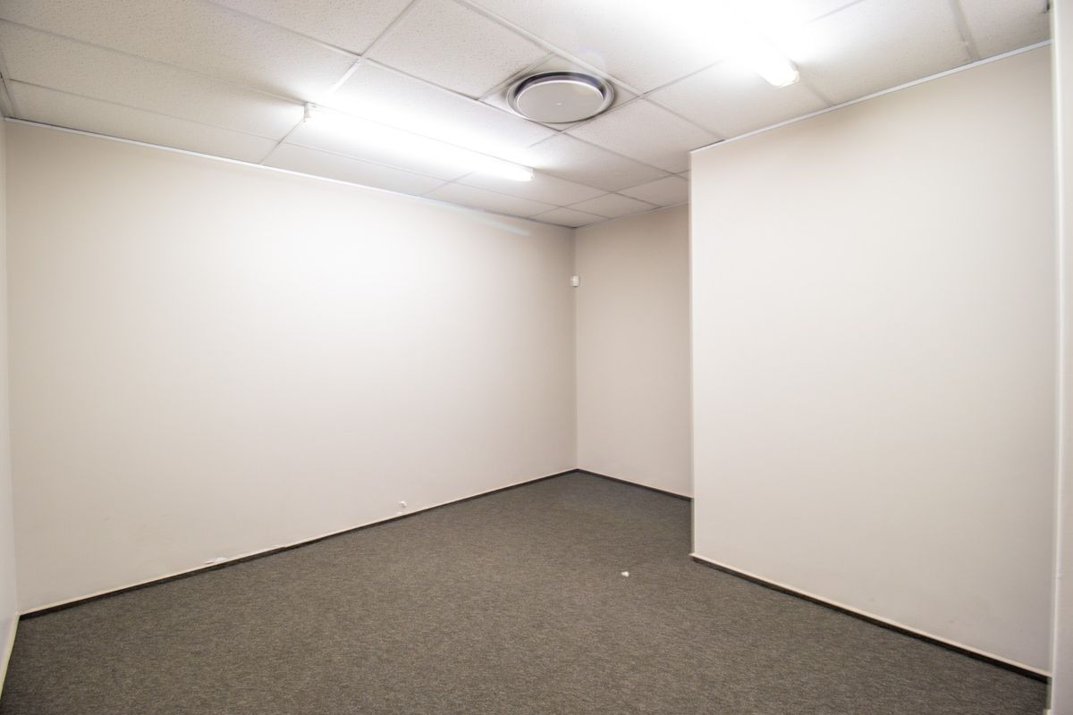 A clean, vacant office space featuring neutral walls, carpeted flooring, and a suspended ceiling with integrated lighting.